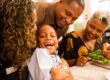 Young child smiling at dinner table surrounded by family of different ages