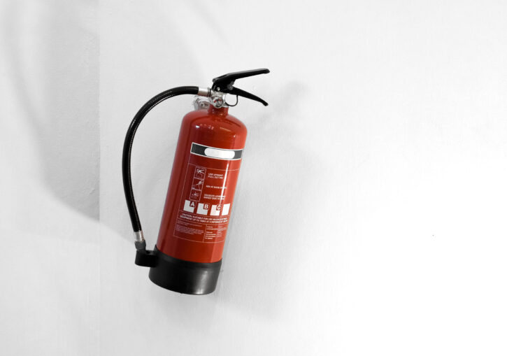 Red fire extinguisher on a white wall fire extinguisher- Prana FM